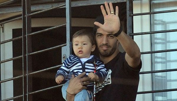 Com os filhos no colo, Surez acena para uruguaios na varanda de casa